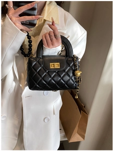 Detail of black quilted leather handbag with gold chain strap and turn-lock closure