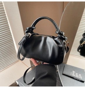 Close-up of black pleated bucket bag with twisted handle and embossed fashion logo