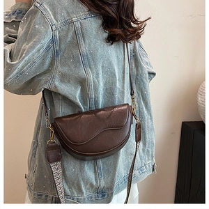Detail of vintage dark brown saddle bag with gold hardware on denim jacket