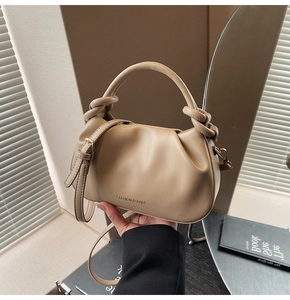 Detail of pleated beige bucket bag featuring a unique knotted handle and fashion lettering