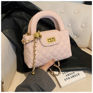 Close-up of light pink quilted handbag with round handle and gold skull charm detail