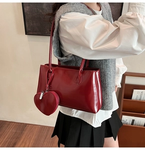 Detail of red patent leather tote bag with heart-shaped charm shown on shoulder