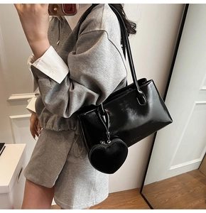 Detail of black glossy leather tote bag featuring a heart-shaped pendant and shoulder strap