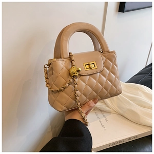 Detailed view of beige quilted handbag with gold turn-lock and leather chain strap