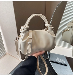 Detail of cream pleated bucket bag featuring decorative knots and gold hardware