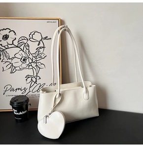 Close-up of beige shoulder tote bag with heart-shaped charm on a minimalist desk