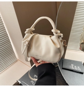 Close-up of cream pleated bucket bag with knotted handle and fashion branding text