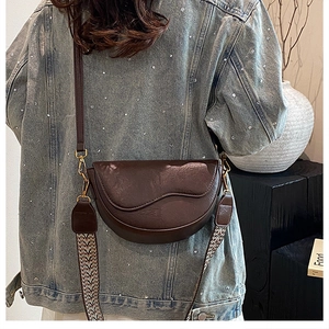 Detail of dark brown half-moon saddle bag featuring a stylish wide woven shoulder strap