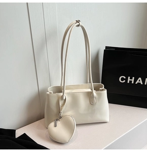 Detail of cream white glossy leather shoulder bag with a heart shaped charm and straps