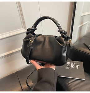 Detail of black pleated bucket bag featuring knotted handle and gold metal hardware