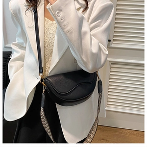 Detail of a black saddle bag with textured leather and gold hardware on two straps