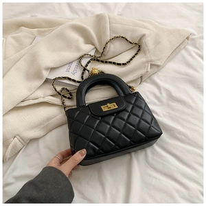 Detailed view of black quilted pattern with gold twist lock and woven chain strap
