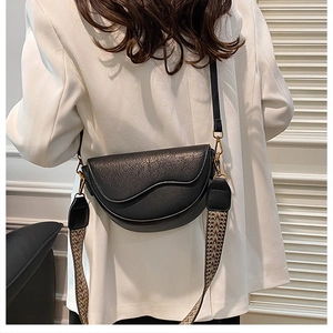 Detail of black saddle bag featuring chic woven strap and gold metal hardware finish