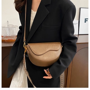 Detail of dark brown saddle bag with textured leather and gold-tone metal buckle strap