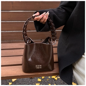 Détail du sac seau en cuir ciré marron foncé avec anse décorative en chaîne à logo métallique
