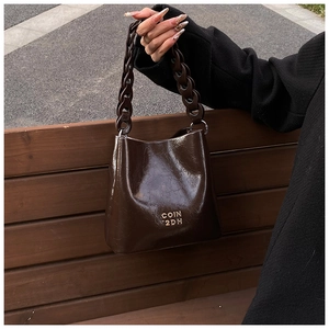 Détail du sac seau en cuir ciré marron foncé avec bandoulière chaîne et logo doré