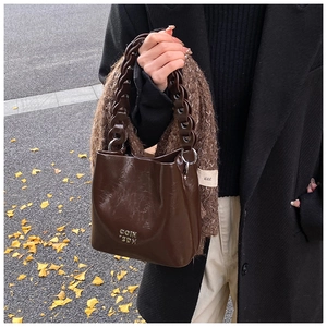 Détail du sac seau marron foncé avec anse chaîne sur un tapis de feuilles de ginkgo