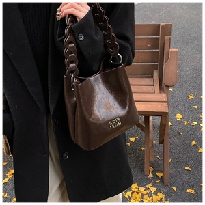 Détail du sac seau en cuir ciré marron foncé avec chaîne en résine et logo doré