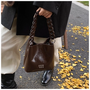 Détail du sac seau en cuir ciré marron foncé avec logo argenté et chaîne en résine