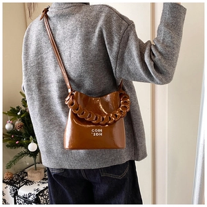 Détail du sac seau en cuir ciré caramel avec bandoulière chaîne et logo décoratif