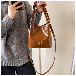 Vue détaillée du sac seau en cuir ciré marron foncé avec anse chaîne et logo embossé