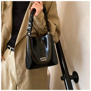 Détail d'un sac seau noir brillant en cuir ciré avec poignée à grosse chaîne