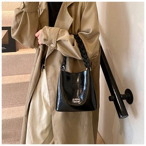 Détail du sac seau en cuir verni noir avec texte COIN 2DH et poignée à grosse chaîne