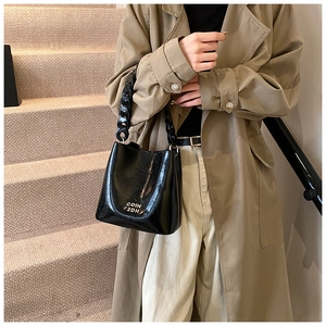 Détail d'un sac seau en cuir verni noir avec lettrage argenté et bandoulière chaîne