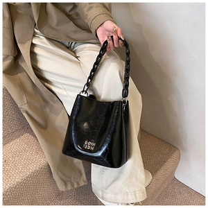 Détail du sac seau noir verni avec poignée chaîne épaisse et lettrage métallique argent
