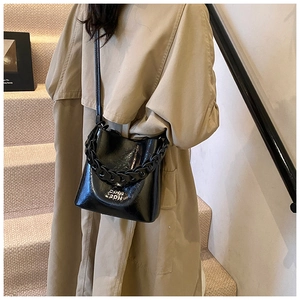 Détail du sac seau noir en cuir ciré vintage avec bandoulière chaîne et logo métallique