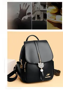 Detail of black pebbled leather backpack featuring golden logo and cat pendant charm