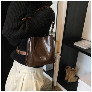 Gros plan du sac seau en cuir ciré marron foncé avec logo doré et bandoulière chaîne