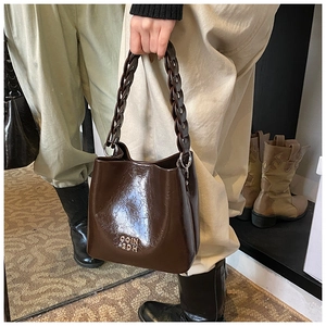 Détail du sac seau en cuir ciré marron foncé avec anse en chaîne tressée et logo