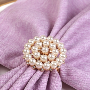Elegant gold napkin ring with white pearls and rhinestones on purple fabric background