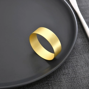 Minimalist matte gold metal napkin rings set on dark textured table for wedding decor