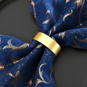 Matte gold minimalist round metal napkin ring displayed on elegant blue patterned fabric