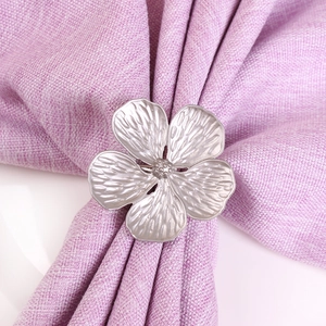 Matte silver five-petal flower napkin ring with fine texture on purple linen background