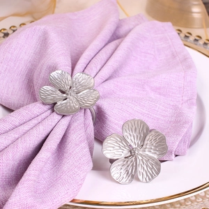 Silver metal floral napkin rings with five-petal flower design on a white dinner plate