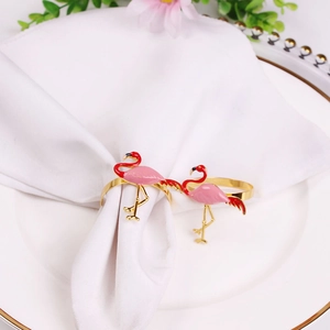 Detailed view of pink enamel flamingo napkin rings on white cloth and gold-rimmed ceramic plate
