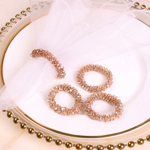 Close-up of four champagne crystal beaded napkin rings on white porcelain decorative plate
