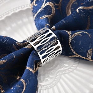 Silver hollow patterned metal napkin ring set on an elegant blue embroidered napkin