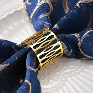 Elegant gold metal napkin ring with hollow oval pattern on a blue embroidered cloth