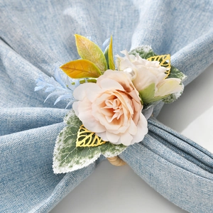 Detail of pink faux rose napkin ring with gold leaves and pearl on blue fabric