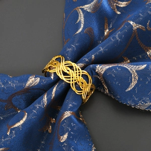Close-up of golden woven napkin ring with intricate layered wave design on blue fabric