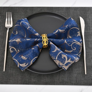 Close-up of golden woven napkin ring with blue baroque pattern napkin on a dinner plate