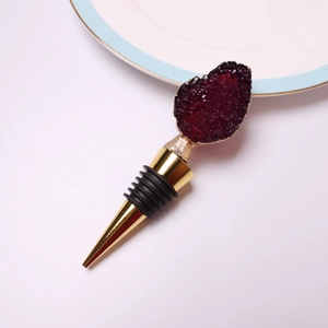 Detail of crystal wine stopper with red geode top and gold metal finish on white