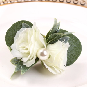 Détail d'un rond de serviette artisanal avec rose en tissu blanc, perle et feuilles vertes