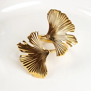 Close-up of golden ginkgo leaf napkin ring with polished metal texture on white plate