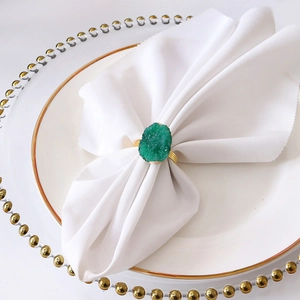Detail of green natural druzy stone with golden spiral napkin ring on a white napkin