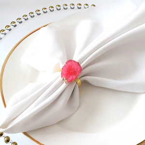 Close-up of golden napkin ring with fuchsia druzy stone on white table setting
